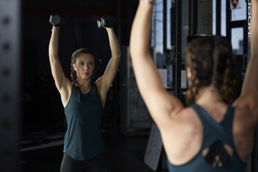 Refection of woman lifting dumbbells at gym seen in mirror - CAVF55019