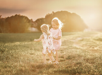 Sisters walking on grassy field against sky during sunset - CAVF55024
