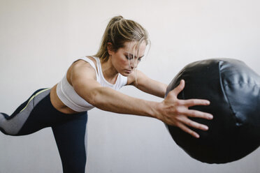 Frau, die einen Fitnessball trägt, während sie an der Wand im Fitnessstudio steht - CAVF55026