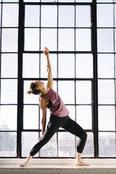 Female athlete practicing yoga by window in gym - CAVF55033