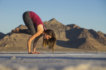 Side view of woman practicing crow pose against clear blue sky during sunset - CAVF55042