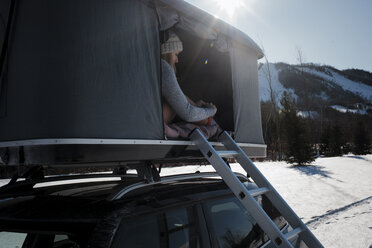 Frau sitzt im Winter im Dachzelt auf dem Auto - CAVF55058