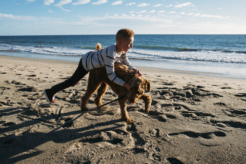 Junge spielt mit Hund am Strand, lizenzfreies Stockfoto