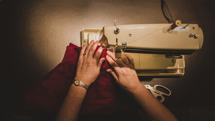 Hochformatiger Ausschnitt der Hände einer Frau, die in einer Werkstatt eine Nähmaschine benutzt - CAVF55109