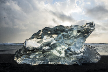 Nahaufnahme eines Eiskristalls am Strand vor bewölktem Himmel - CAVF55119