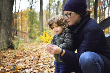 Mutter zeigt ihrem Sohn ein Blatt, während sie im Herbst auf einem Feld hockt - CAVF55134