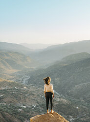 Rückansicht einer Frau, die auf einem Felsen stehend die Berge gegen den klaren Himmel betrachtet - CAVF55175