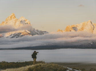 Seitenansicht eines Wanderers, der mit der Kamera fotografiert, während er vor den Bergen steht - CAVF55179
