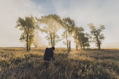 Rückansicht eines Wanderers beim Einstellen des Stativs im Feld - CAVF55181