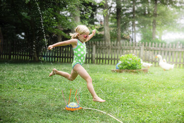 Seitenansicht eines Mädchens in Badekleidung, das über Sprinkleranlagen im Hof läuft - CAVF55188