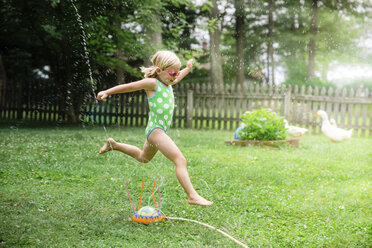 Side view of girl in swimwear running over sprinklers at yard - CAVF55188