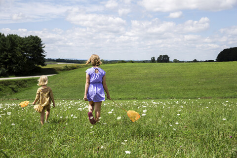Rückansicht von Schwestern, die auf einem grasbewachsenen Feld gegen einen bewölkten Himmel laufen, lizenzfreies Stockfoto