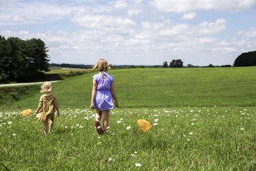 Rückansicht von Schwestern, die auf einem grasbewachsenen Feld gegen einen bewölkten Himmel laufen - CAVF55190