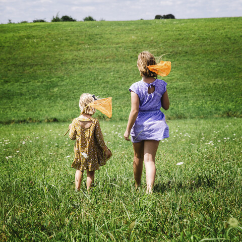 Rückansicht von Schwestern, die auf einem grasbewachsenen Feld gehen, lizenzfreies Stockfoto