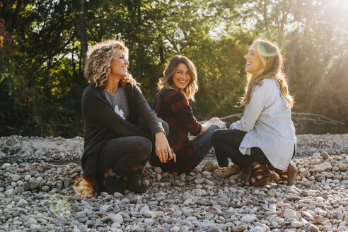 Glückliche Freundinnen sitzen auf Kieselsteinen an einem sonnigen Tag - CAVF55220