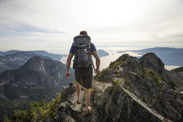 Rückansicht eines Wanderers mit Rucksack, der auf einem Berg gegen den Himmel läuft - CAVF55253