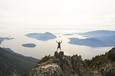 High angle view of hiker with arms raised standing on mountain against sky - CAVF55258