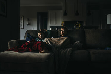 Brothers under blankets watching TV while sitting on sofa at home in darkroom - CAVF55267