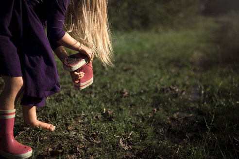 Mädchen entfernt Schmutz aus einem Gummistiefel auf einem Feld im Park - CAVF55313
