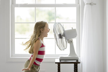Side view of playful girl screaming in front of windy electric fan - CAVF55318