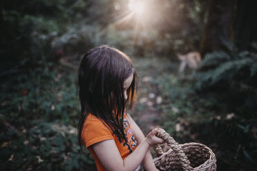 Side view of girl with wicker basket standing at forest - CAVF55339