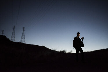 Mann, der sein Smartphone benutzt, während er in der Abenddämmerung vor einem klaren Himmel steht - CAVF55345