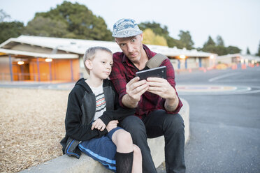 Vater und Sohn sprechen Selfie durch Handy beim Sitzen auf der Straße - CAVF55351