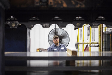 Porträt eines Arbeiters, der in einer Fabrik der Stahlindustrie vor Metallplatten steht - CAVF55382
