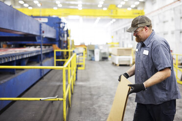 Lächelnder Arbeiter, der Metallbleche bei der Arbeit in einer Stahlindustrie-Fabrik hält - CAVF55395