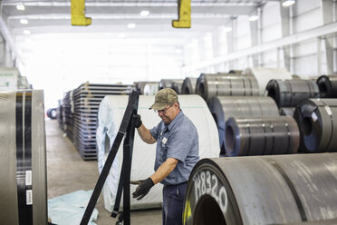 Seitenansicht eines Arbeiters, der bei der Arbeit in einer Fabrik vor einem aufgerollten Metallblech steht - CAVF55427