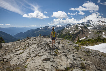 Rear view of female hiker walking on rock formations against mountains and cloudy sky during winter at North Cascades National Park - CAVF55439