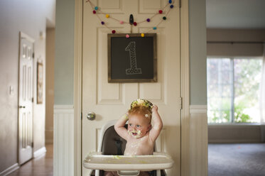 Baby-Junge spielt mit Kuchen, während auf Hochstuhl zu Hause während Geburtstag sitzen - CAVF55451