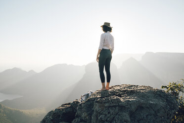 Rückansicht einer Frau, die auf einem Felsen stehend die Aussicht gegen den Himmel betrachtet, an einem sonnigen Tag - CAVF55463