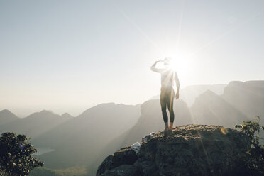 Rückansicht einer Frau, die die Berge betrachtet, während sie auf einem Felsen gegen den Himmel an einem sonnigen Tag steht - CAVF55464