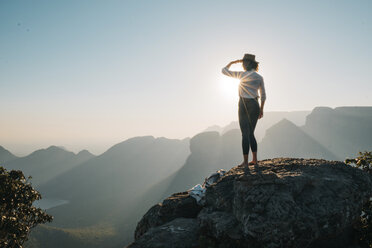 Rückansicht einer Frau, die an einem sonnigen Tag auf einem Felsen stehend die Berge betrachtet - CAVF55465