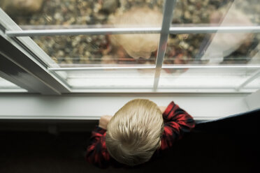 Hoher Blickwinkel des kleinen Jungen, der durch das Fenster schaut, während er zu Hause steht - CAVF55479