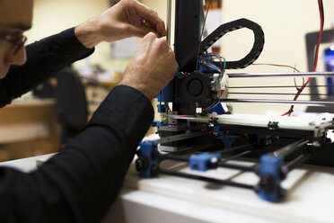 Männlicher Ingenieur, der einen 3D-Drucker auf einem Tisch befestigt - CAVF55535