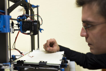 Confident engineer examining 3D printer on table - CAVF55536