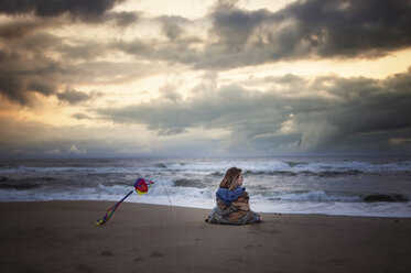 Mädchen betrachtet die Aussicht, während sie in eine Decke eingewickelt am Ufer gegen stürmische Wolken steht - CAVF55540