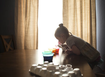 Side view of girl preparing Easter eggs on table at home - CAVF55542