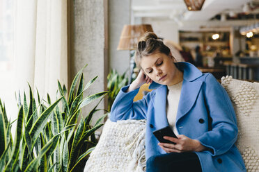 Young woman wearing trench coat while using smart phone at cafe - CAVF55549