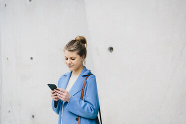 Junge Frau benutzt ihr Smartphone, während sie in der Stadt an der Wand steht - CAVF55564