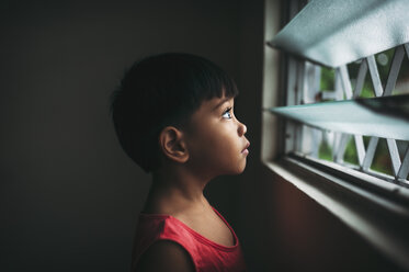 Seitenansicht eines Jungen, der durch ein Fenster schaut, während er zu Hause steht - CAVF55583