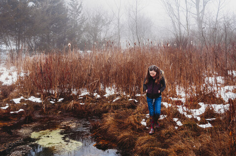 Mädchen geht im Winter auf einer Wiese am See im Wald spazieren, lizenzfreies Stockfoto