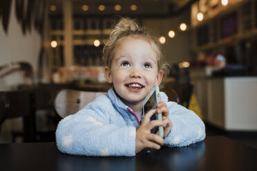 Close-up of smiling girl holding smart phone while sitting at table in restaurant - CAVF55595