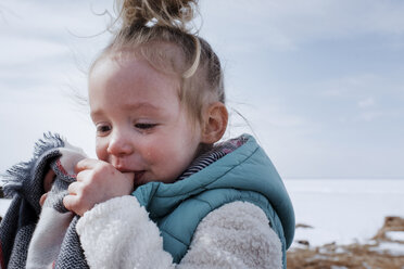 Close-up of crying girl sucking thumbs while standing against sky during winter - CAVF55603