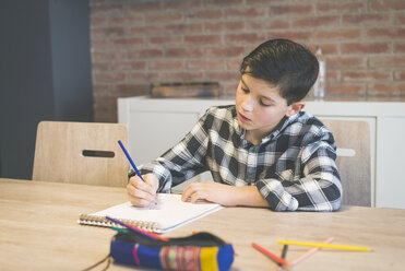 Boy coloring on spiral notebook with colored pencil at table in home - CAVF55604