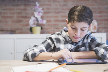 Boy sticking out tongue while drawing on tablet computer at table - CAVF55606