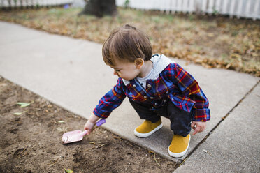 Baby-Junge spielt mit Spielzeug-Schaufel, während er auf dem Rasen hockt - CAVF55621