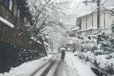 Rückansicht einer Frau, die einen Regenschirm hält, während sie auf einer schneebedeckten Straße bei Schneefall in der Stadt geht - CAVF55635